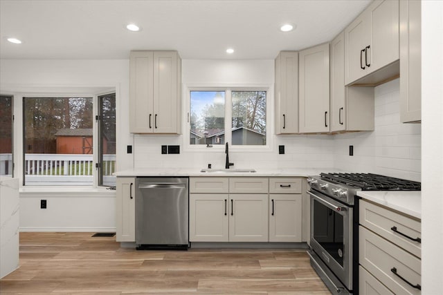 kitchen featuring light stone counters, sink, stainless steel appliances, and light hardwood / wood-style floors