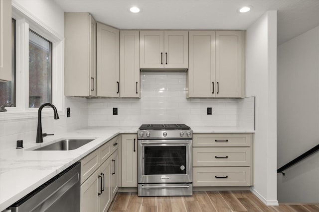 kitchen featuring decorative backsplash, light stone countertops, sink, and appliances with stainless steel finishes