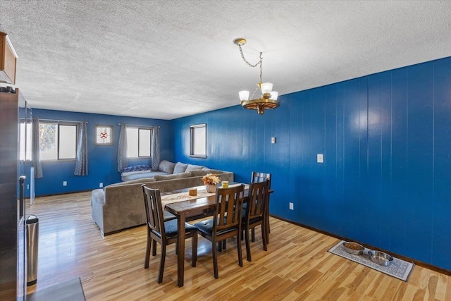 dining room with light wood-type flooring, a textured ceiling, and an inviting chandelier