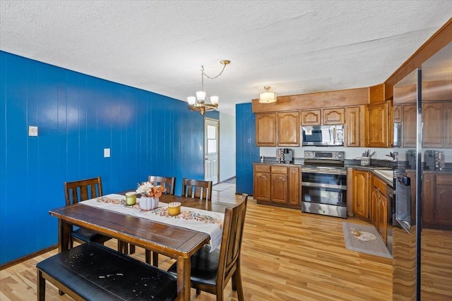 kitchen with light wood-type flooring, a textured ceiling, stainless steel appliances, pendant lighting, and a chandelier