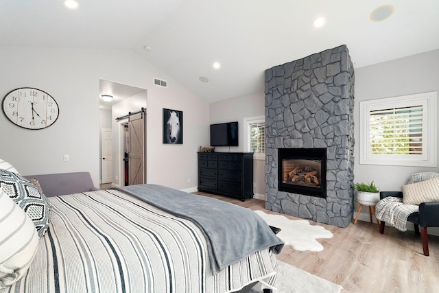 bedroom featuring a barn door, a fireplace, light hardwood / wood-style floors, and vaulted ceiling