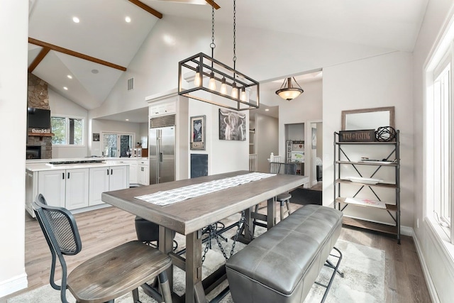 dining space featuring beam ceiling, a fireplace, high vaulted ceiling, and light hardwood / wood-style floors