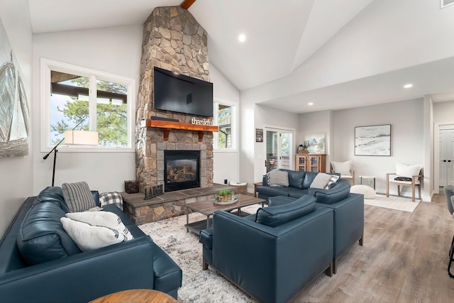 living room featuring hardwood / wood-style flooring, a stone fireplace, beamed ceiling, and high vaulted ceiling