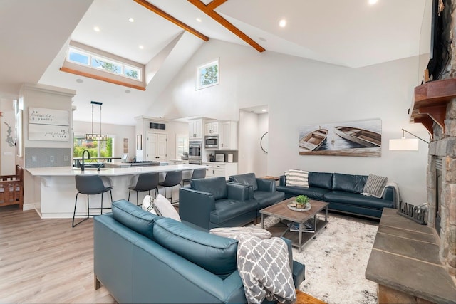 living room with beamed ceiling, light wood-type flooring, high vaulted ceiling, and sink