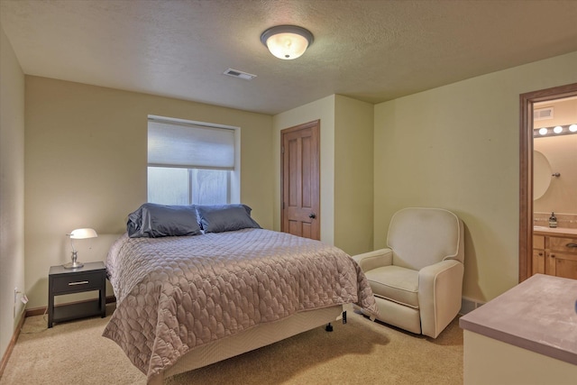 carpeted bedroom featuring ensuite bathroom and a textured ceiling