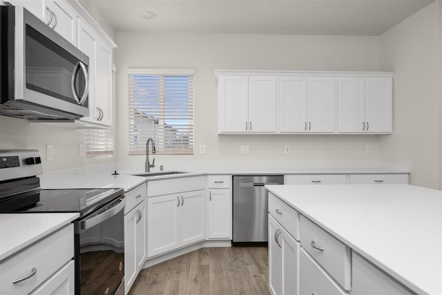 kitchen with sink, white cabinets, light hardwood / wood-style floors, and appliances with stainless steel finishes