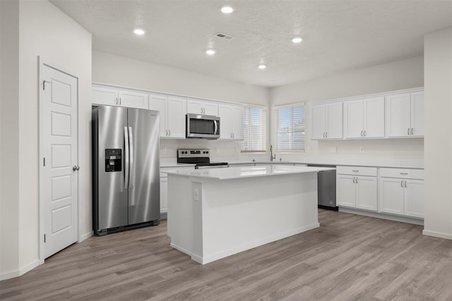 kitchen with light wood-type flooring, appliances with stainless steel finishes, a center island, and white cabinetry