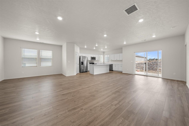 unfurnished living room with a textured ceiling, light hardwood / wood-style floors, plenty of natural light, and sink