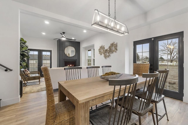 dining space featuring french doors, light wood-type flooring, a large fireplace, and plenty of natural light