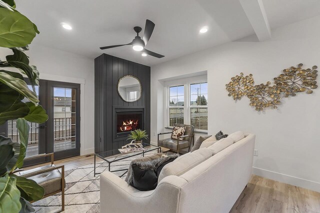 living room with beamed ceiling, ceiling fan, a large fireplace, and light wood-type flooring