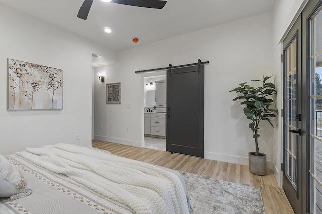 bedroom featuring access to exterior, ensuite bath, ceiling fan, a barn door, and light hardwood / wood-style floors