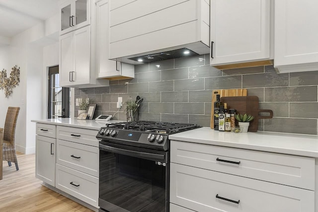 kitchen with white cabinetry, gas range oven, premium range hood, light hardwood / wood-style floors, and decorative backsplash