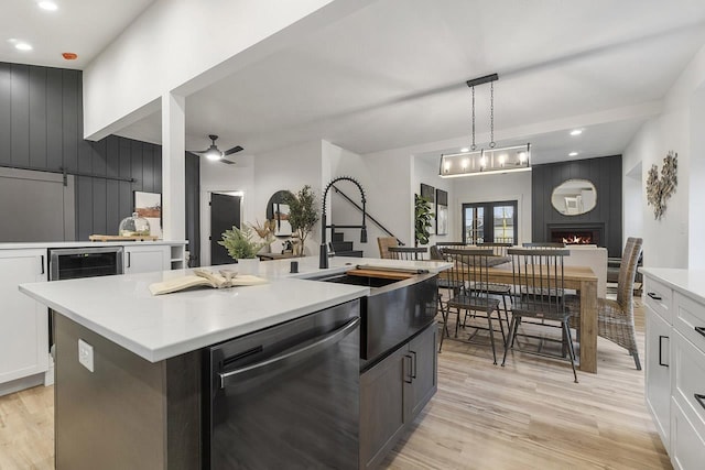 kitchen with stainless steel dishwasher, ceiling fan, sink, white cabinets, and an island with sink