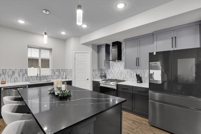 kitchen featuring hanging light fixtures, sink, hardwood / wood-style flooring, wall chimney exhaust hood, and appliances with stainless steel finishes