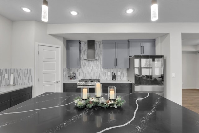 kitchen featuring stainless steel range, hanging light fixtures, wall chimney range hood, dark stone countertops, and refrigerator