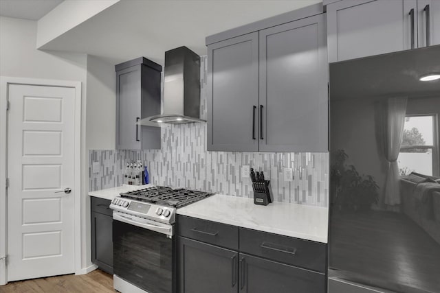 kitchen with stainless steel range with gas cooktop, gray cabinetry, wall chimney range hood, and light hardwood / wood-style flooring