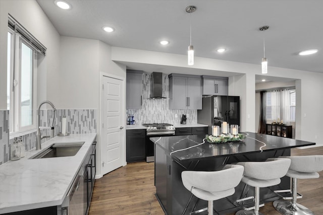 kitchen featuring appliances with stainless steel finishes, backsplash, sink, wall chimney range hood, and hanging light fixtures