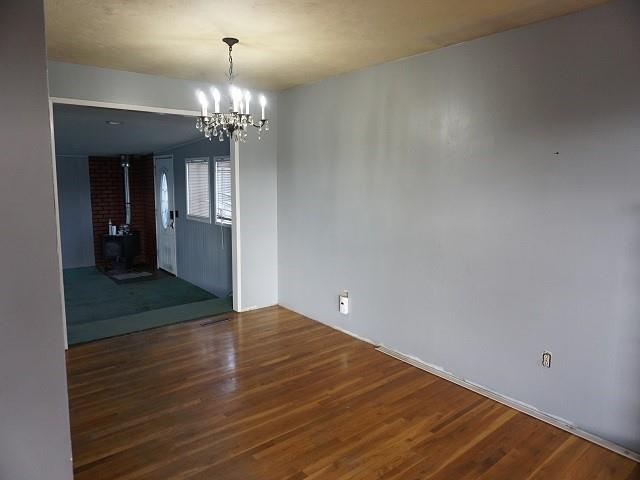 unfurnished dining area with a wood stove, dark hardwood / wood-style floors, and a notable chandelier