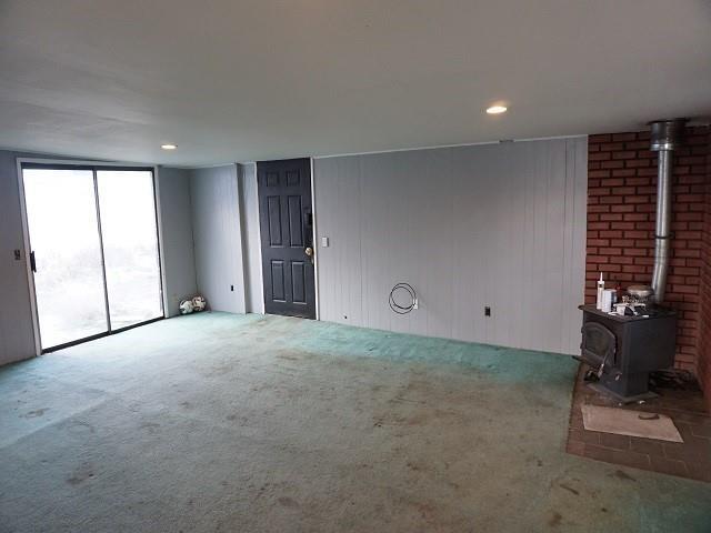 unfurnished living room featuring a wood stove and light colored carpet