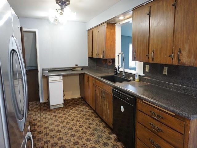 kitchen featuring backsplash, black dishwasher, sink, and stainless steel refrigerator