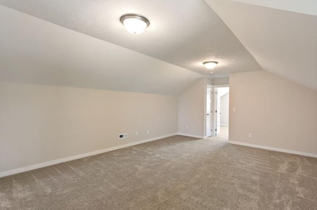 additional living space with carpet, a textured ceiling, and vaulted ceiling