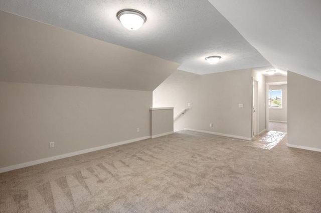 additional living space with a textured ceiling, lofted ceiling, and light carpet