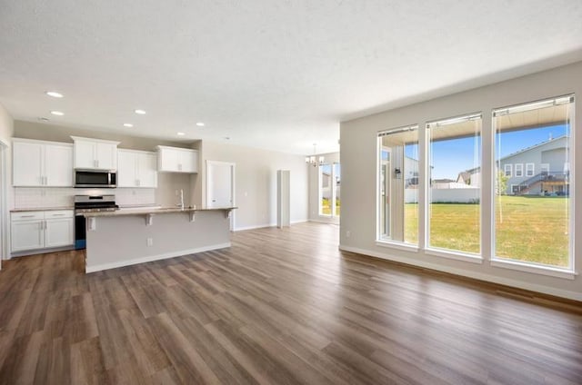 kitchen featuring a breakfast bar, a kitchen island with sink, a notable chandelier, white cabinetry, and stainless steel appliances