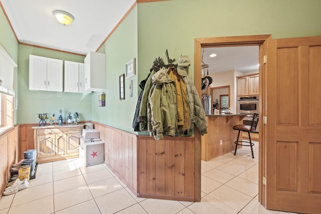 kitchen featuring wood walls, light tile patterned floors, white cabinetry, kitchen peninsula, and a breakfast bar area