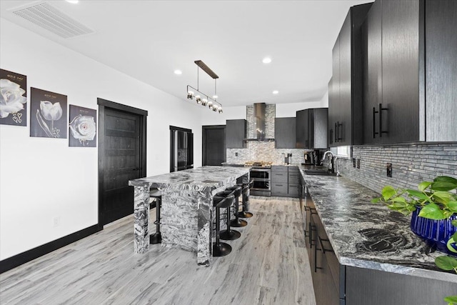 kitchen with a breakfast bar, wall chimney range hood, sink, decorative backsplash, and decorative light fixtures