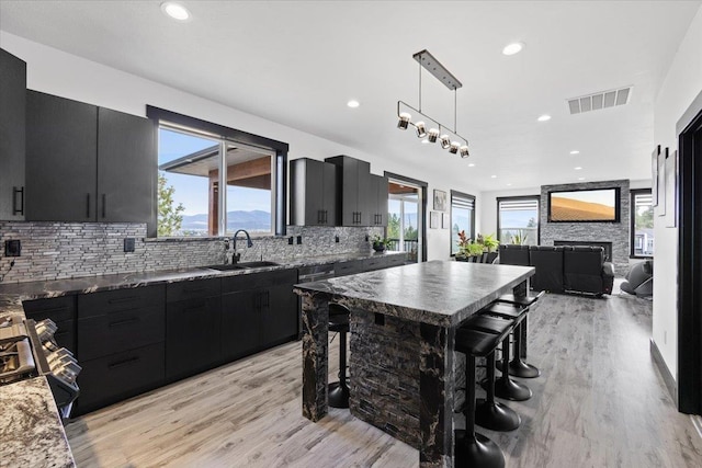 kitchen with pendant lighting, a kitchen breakfast bar, sink, light hardwood / wood-style flooring, and tasteful backsplash