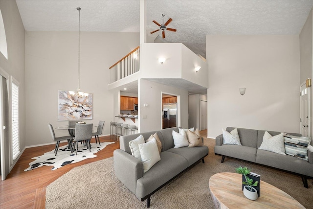 living room featuring ceiling fan with notable chandelier, light hardwood / wood-style floors, a textured ceiling, and high vaulted ceiling