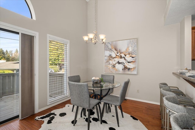 dining area featuring a towering ceiling, wood-type flooring, and a notable chandelier