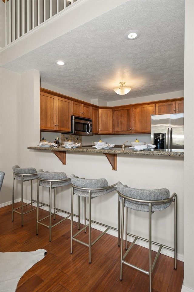 kitchen with a kitchen bar, appliances with stainless steel finishes, kitchen peninsula, and light stone counters