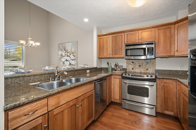 kitchen featuring sink, an inviting chandelier, dark hardwood / wood-style flooring, dark stone countertops, and appliances with stainless steel finishes