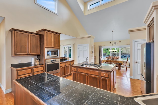 kitchen featuring appliances with stainless steel finishes, plenty of natural light, high vaulted ceiling, a center island, and hanging light fixtures