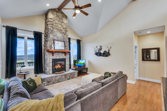 living room with lofted ceiling with beams, ceiling fan, a stone fireplace, and light hardwood / wood-style flooring