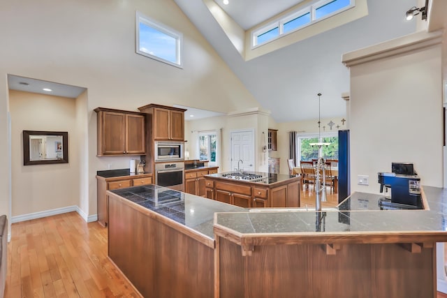 kitchen with stainless steel appliances, a high ceiling, light hardwood / wood-style flooring, kitchen peninsula, and a kitchen bar