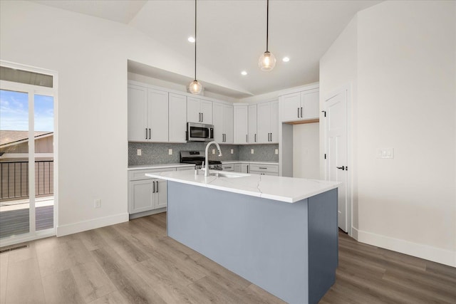 4217 W Tolliver Ct, Spokane, WA 99208 - kitchen with stainless steel microwave, vaulted ceiling, light wood finished floors, backsplash, and a center island with sink