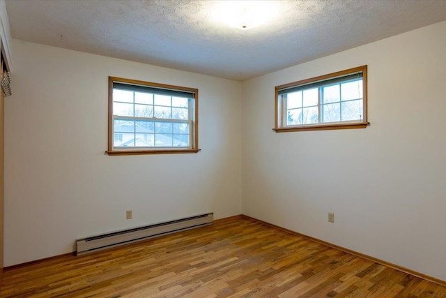 spare room with a wealth of natural light, light hardwood / wood-style flooring, a textured ceiling, and a baseboard heating unit