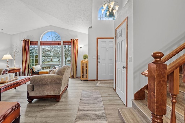 foyer entrance featuring a textured ceiling, light wood-type flooring, an inviting chandelier, and lofted ceiling