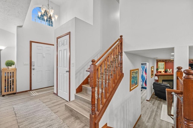 foyer with a textured ceiling, a chandelier, a high ceiling, and light wood-type flooring