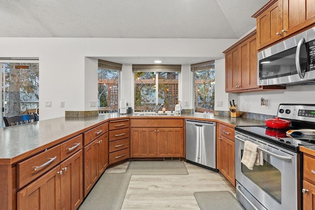 kitchen with sink, kitchen peninsula, light hardwood / wood-style floors, a textured ceiling, and appliances with stainless steel finishes