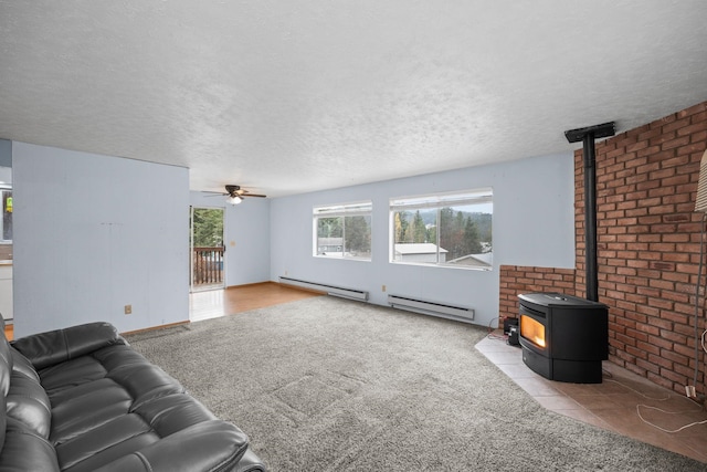 living room featuring ceiling fan, a wood stove, light carpet, and a baseboard heating unit