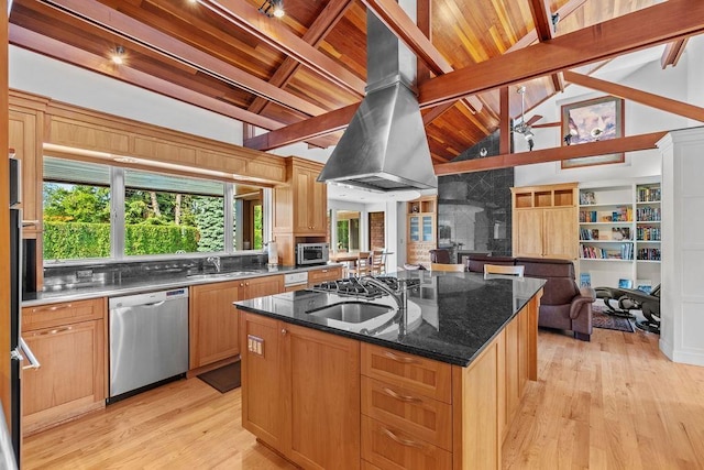 kitchen with stainless steel appliances, range hood, an island with sink, dark stone counters, and light wood-type flooring