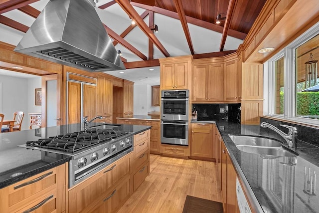 kitchen with island exhaust hood, appliances with stainless steel finishes, sink, dark stone countertops, and vaulted ceiling with beams