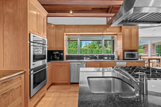 kitchen with dark stone counters, sink, stainless steel appliances, and wall chimney range hood