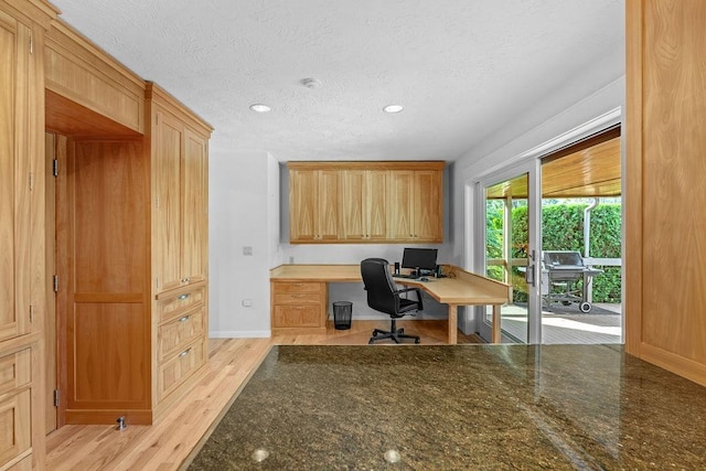 office area with light wood-type flooring, built in desk, and a textured ceiling