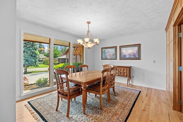 dining space with a textured ceiling, light hardwood / wood-style flooring, an inviting chandelier, and a wealth of natural light