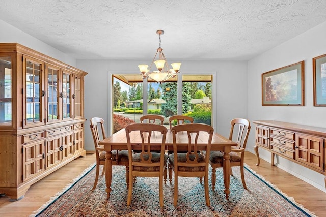 dining space with a textured ceiling, light hardwood / wood-style flooring, and an inviting chandelier