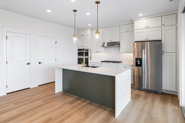 4706 W Lex Ave Lot 5, Spokane, WA 99208 - kitchen with appliances with stainless steel finishes, under cabinet range hood, decorative backsplash, light wood-style flooring, and a kitchen island with sink